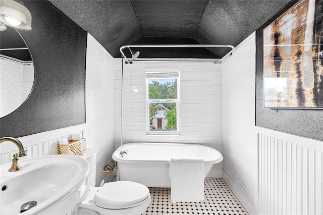 bathroom with wainscoting, a sink, a freestanding tub, vaulted ceiling, and a textured wall