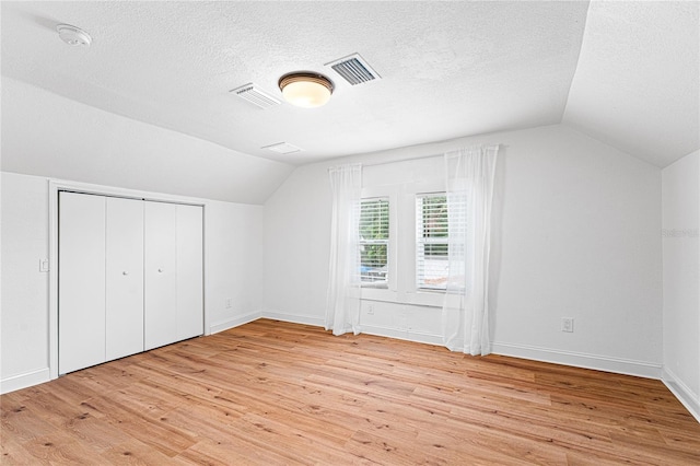 additional living space with a textured ceiling, light wood-type flooring, and lofted ceiling