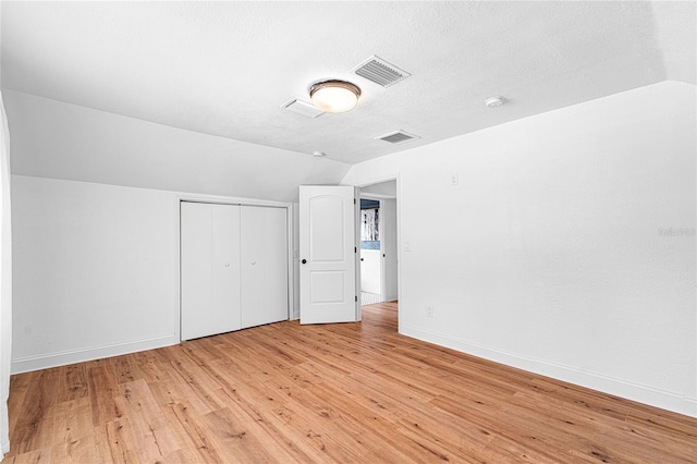 unfurnished bedroom featuring a closet, vaulted ceiling, light hardwood / wood-style floors, and a textured ceiling