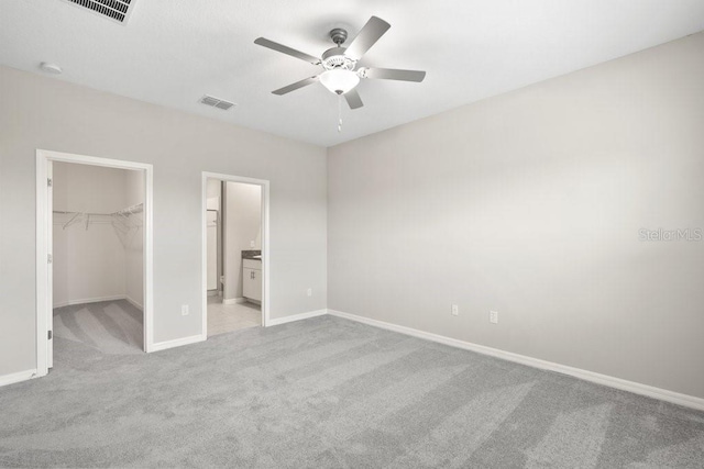 unfurnished bedroom featuring light carpet, connected bathroom, ceiling fan, a closet, and a spacious closet