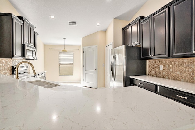 kitchen featuring light stone countertops, appliances with stainless steel finishes, backsplash, a textured ceiling, and decorative light fixtures