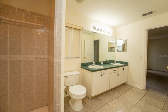 bathroom featuring toilet, tiled shower, vanity, and tile patterned floors