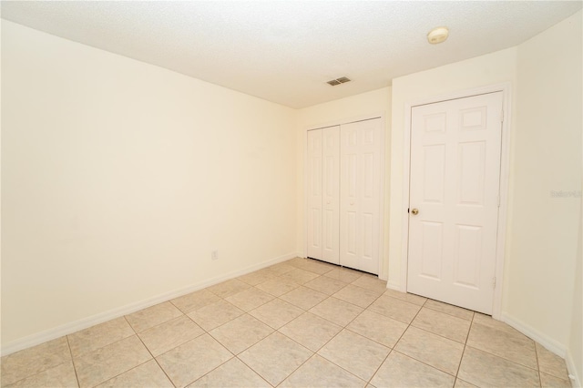 unfurnished bedroom featuring a textured ceiling, light tile patterned floors, and a closet