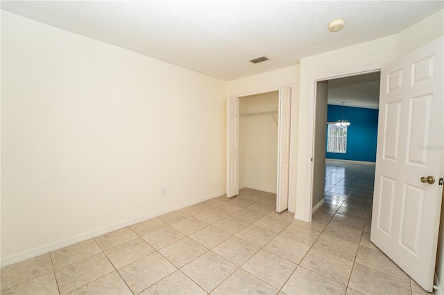 unfurnished bedroom with a closet, an inviting chandelier, a textured ceiling, and light tile patterned floors