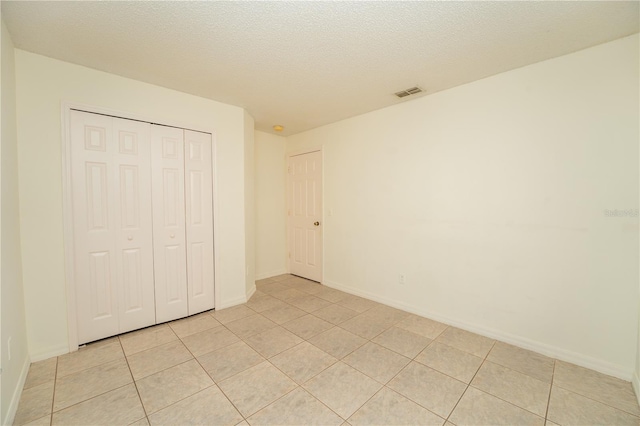 unfurnished bedroom with a closet, a textured ceiling, and light tile patterned floors