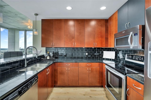 kitchen featuring appliances with stainless steel finishes, decorative light fixtures, sink, dark stone counters, and light hardwood / wood-style flooring