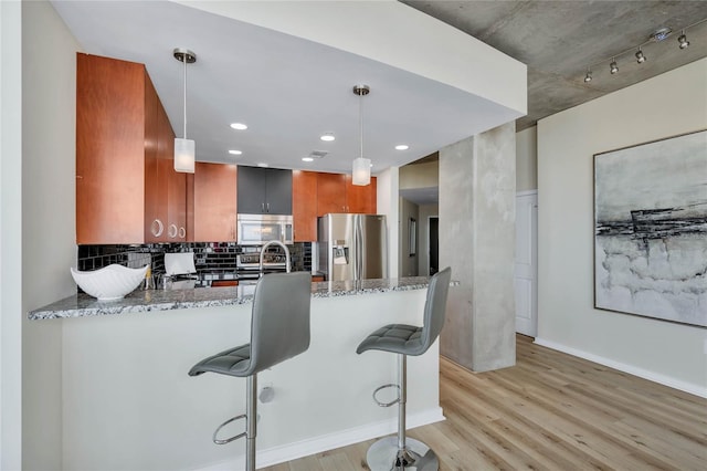 kitchen featuring stainless steel appliances, light stone countertops, kitchen peninsula, and decorative light fixtures