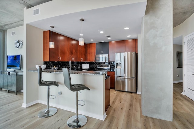 kitchen featuring a breakfast bar, light hardwood / wood-style flooring, kitchen peninsula, pendant lighting, and stainless steel appliances