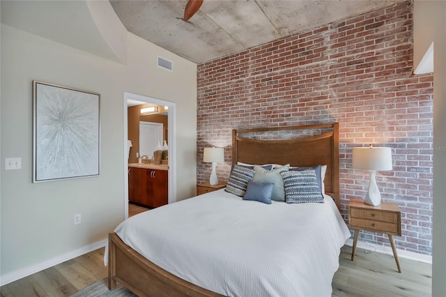 bedroom with brick wall, connected bathroom, and light hardwood / wood-style flooring