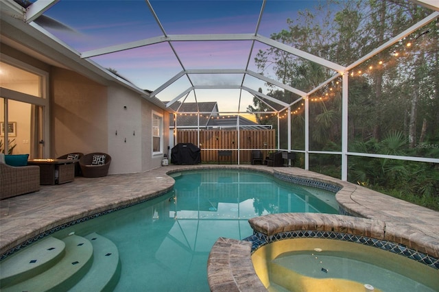 pool at dusk with an in ground hot tub, a lanai, and a patio area