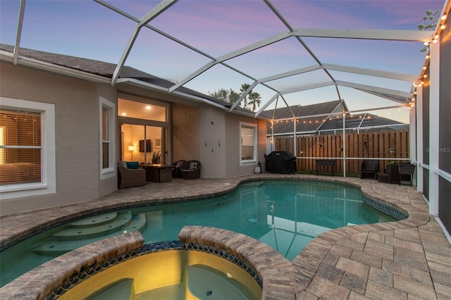 pool at dusk with glass enclosure, an in ground hot tub, a patio, and grilling area