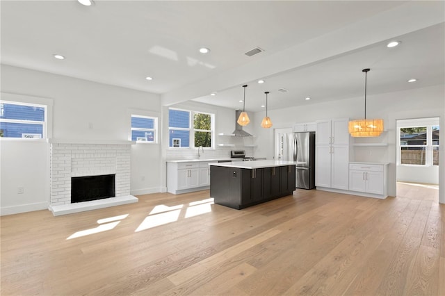 kitchen with a center island, wall chimney exhaust hood, pendant lighting, light wood-type flooring, and appliances with stainless steel finishes