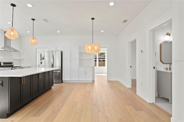 kitchen with stainless steel appliances, light hardwood / wood-style floors, wall chimney range hood, and hanging light fixtures