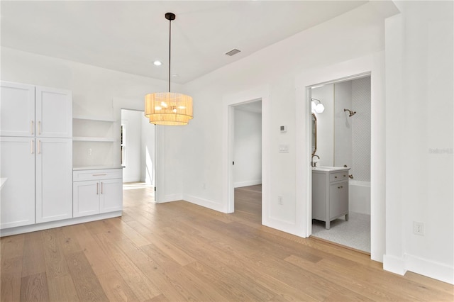 unfurnished dining area with an inviting chandelier, sink, and light wood-type flooring