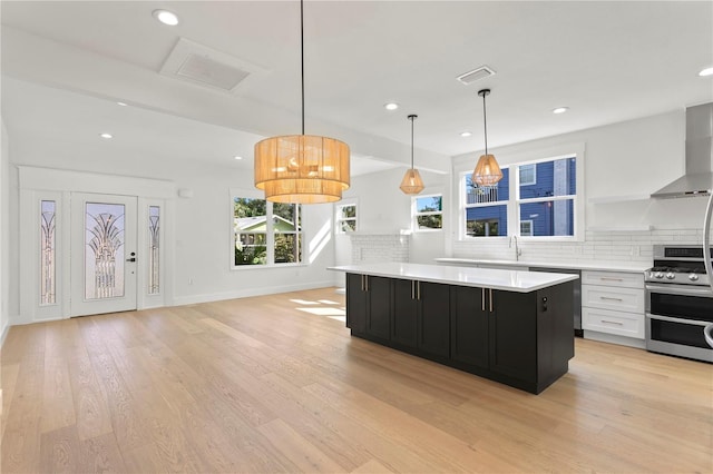 kitchen featuring tasteful backsplash, wall chimney exhaust hood, light hardwood / wood-style flooring, white cabinets, and stainless steel stove