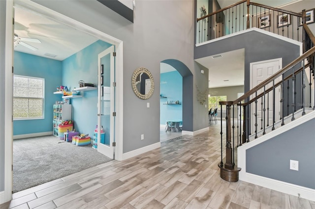 entryway with wood-type flooring, ceiling fan, and a towering ceiling