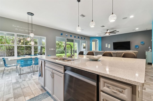 kitchen with a center island with sink, light stone countertops, stainless steel dishwasher, hanging light fixtures, and light wood-type flooring