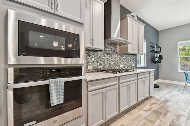 kitchen with white cabinetry, light stone counters, appliances with stainless steel finishes, tasteful backsplash, and wall chimney exhaust hood