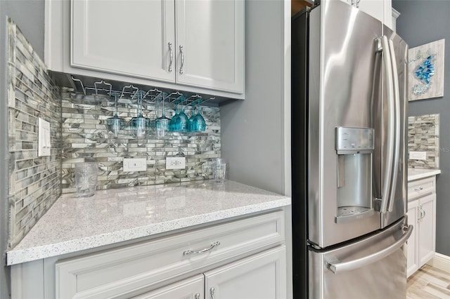 kitchen featuring white cabinetry, stainless steel refrigerator with ice dispenser, backsplash, and light stone countertops