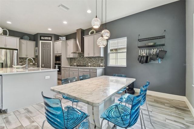 kitchen with white cabinets, wall chimney exhaust hood, a kitchen island with sink, and appliances with stainless steel finishes