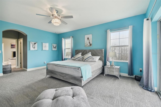 carpeted bedroom featuring ensuite bathroom, ceiling fan, and multiple windows