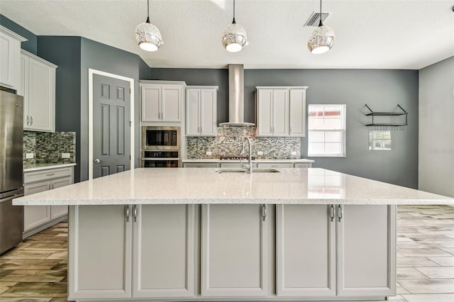 6317 Brevada Ln, Apollo Beach, FL 33572 - kitchen featuring wall chimney range hood, stainless steel appliances, a sink, decorative backsplash, and a spacious island