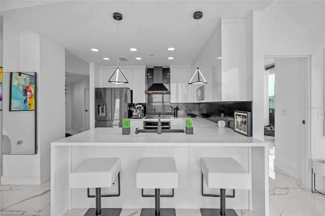 kitchen with wall chimney exhaust hood, a kitchen bar, stainless steel fridge, kitchen peninsula, and pendant lighting