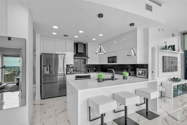 kitchen with wall chimney exhaust hood, a breakfast bar, decorative light fixtures, black appliances, and white cabinets