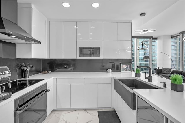 kitchen featuring white cabinetry, backsplash, black appliances, decorative light fixtures, and wall chimney exhaust hood