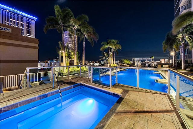 pool at twilight with a hot tub and a patio