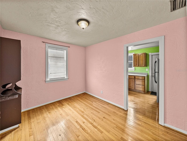 empty room with light wood-type flooring and a textured ceiling