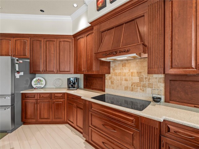 kitchen featuring black electric stovetop, decorative backsplash, ornamental molding, custom range hood, and stainless steel fridge