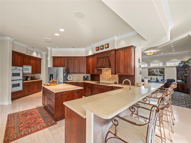 kitchen with a kitchen bar, kitchen peninsula, premium range hood, and white appliances