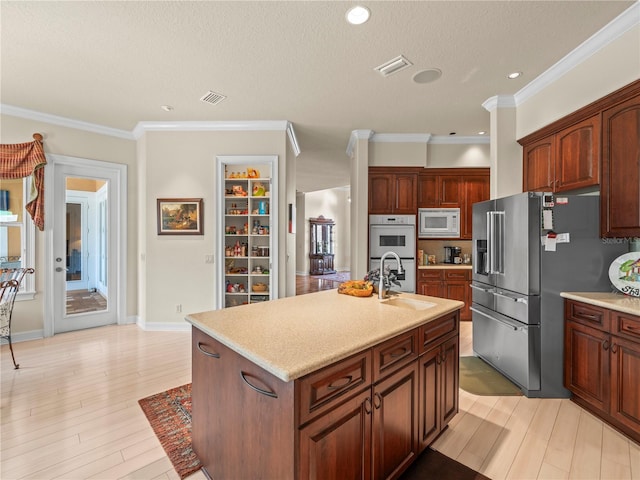 kitchen featuring a center island with sink, a textured ceiling, ornamental molding, light hardwood / wood-style flooring, and white appliances