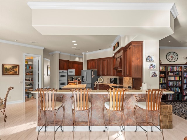 kitchen featuring crown molding, white appliances, a kitchen breakfast bar, kitchen peninsula, and light hardwood / wood-style flooring