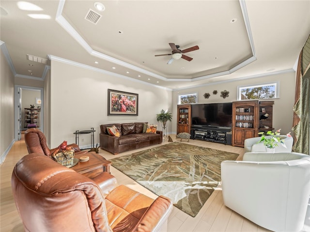 living room with light hardwood / wood-style floors, ceiling fan, ornamental molding, and a tray ceiling