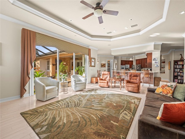 living room featuring light hardwood / wood-style floors, ceiling fan, crown molding, and a tray ceiling