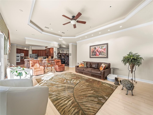 living room with light hardwood / wood-style floors, ceiling fan, crown molding, and a tray ceiling