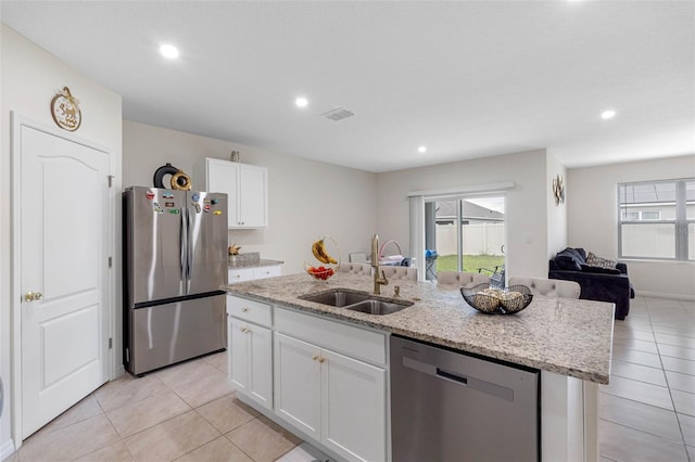 kitchen featuring a center island with sink, white cabinetry, appliances with stainless steel finishes, light stone countertops, and sink