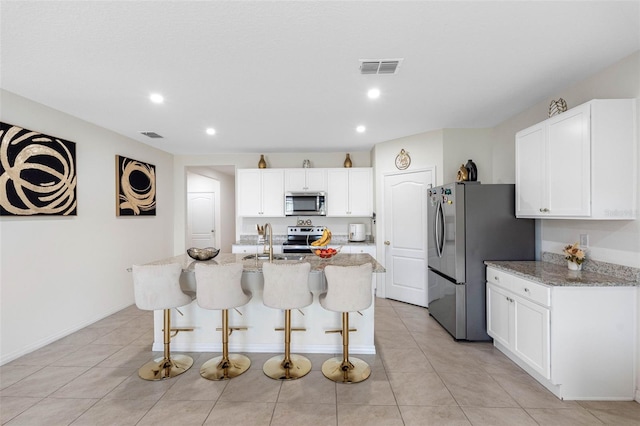 kitchen featuring white cabinetry, appliances with stainless steel finishes, a center island with sink, and light stone countertops