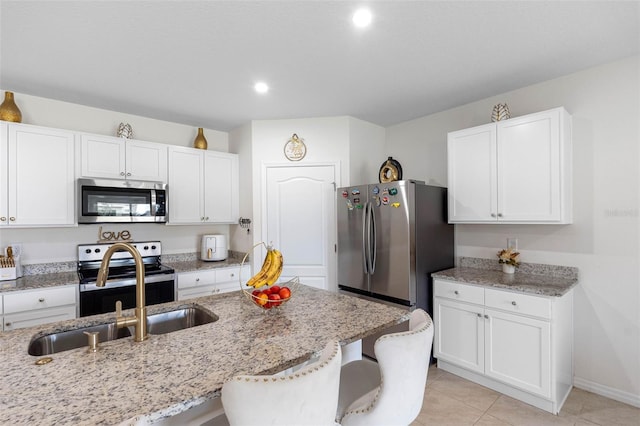 kitchen with a kitchen bar, stainless steel appliances, white cabinets, and light stone countertops