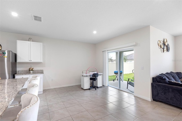 kitchen with white cabinetry, light stone countertops, light tile patterned floors, and stainless steel fridge