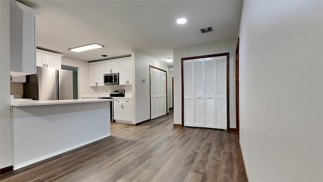 kitchen featuring kitchen peninsula, white cabinets, dark wood-type flooring, and appliances with stainless steel finishes