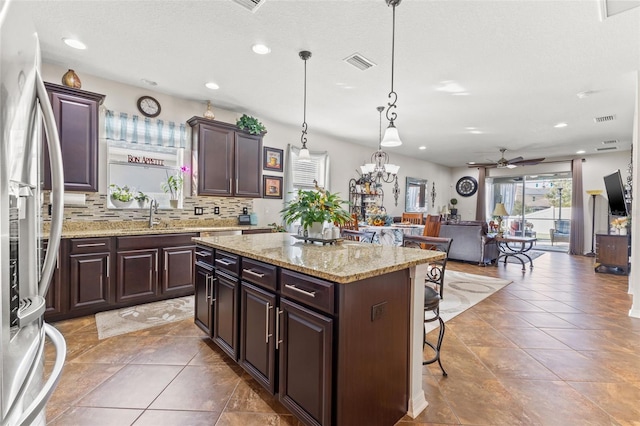 kitchen with stainless steel fridge, hanging light fixtures, a center island, and dark brown cabinetry