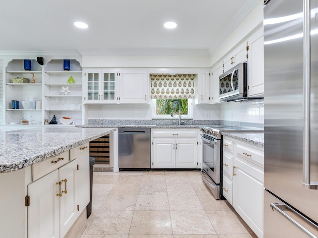 kitchen featuring stainless steel appliances, white cabinetry, sink, light stone counters, and ornamental molding