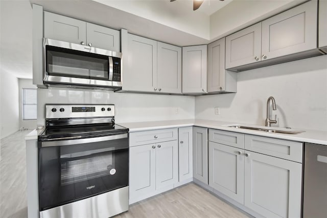 kitchen featuring sink, gray cabinets, ceiling fan, light wood-type flooring, and appliances with stainless steel finishes