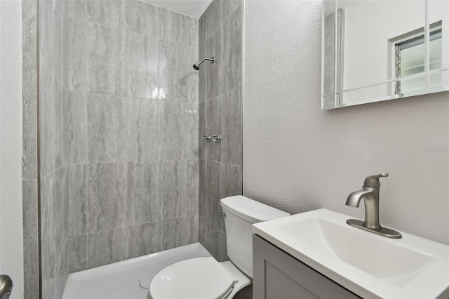 bathroom with a tile shower, vanity, and toilet