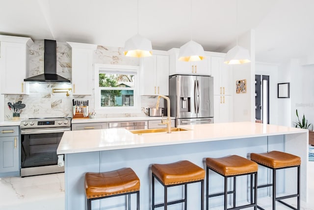 kitchen with a kitchen island with sink, appliances with stainless steel finishes, wall chimney exhaust hood, and decorative light fixtures