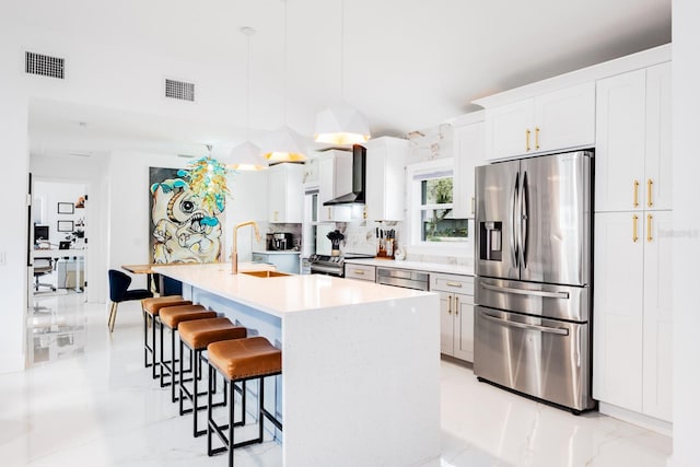 kitchen featuring white cabinets, hanging light fixtures, an island with sink, and stainless steel appliances