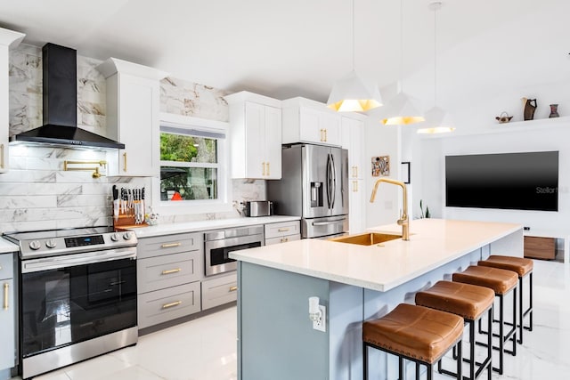 kitchen with stainless steel appliances, wall chimney range hood, pendant lighting, sink, and an island with sink